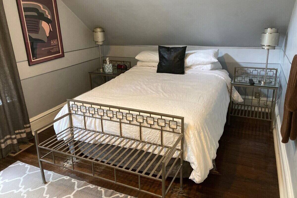 A bedroom with a metal bed frame, white bedding, a black pillow, bedside tables with lamps, and a framed picture on the wall.