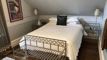 A bedroom with a metal bed frame, white bedding, a black pillow, bedside tables with lamps, and a framed picture on the wall.
