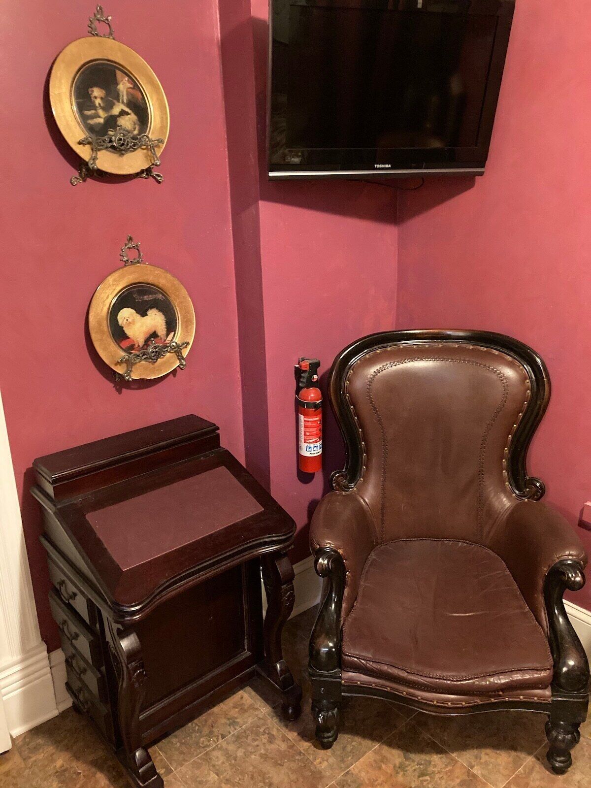 A room with a brown leather armchair, a small wooden table, and two framed pictures on the wall.