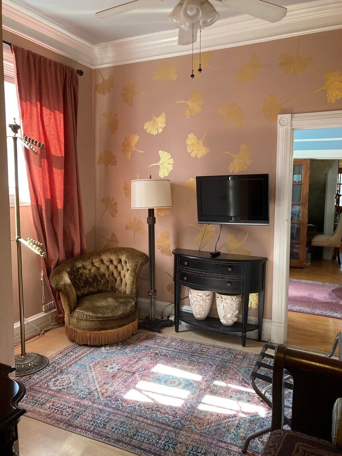 A room with a tufted armchair, a standing lamp, a television on a black stand, and a patterned rug.