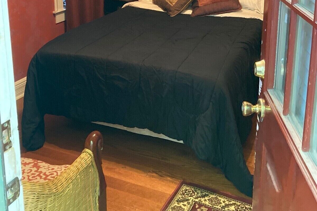 A bedroom with a bed, a nightstand, a lamp, a wall hanging, and a chair.