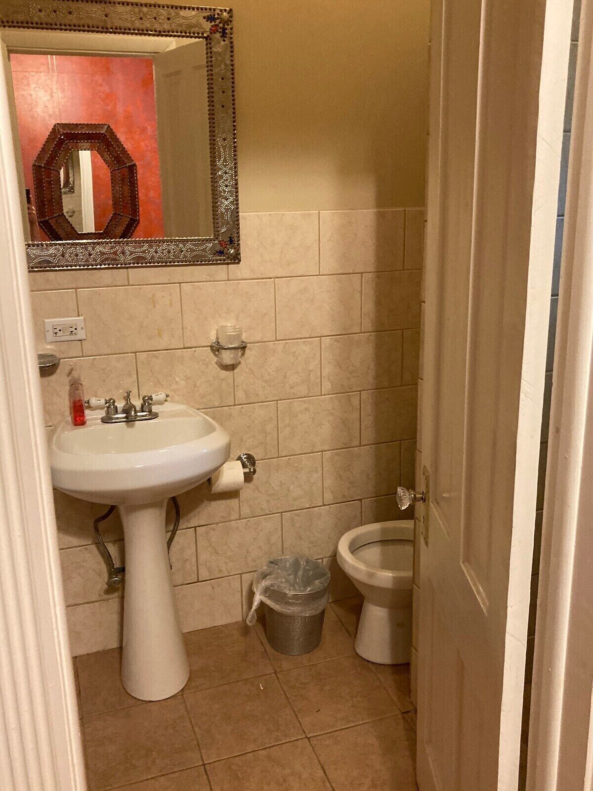 A small bathroom with a pedestal sink, a toilet, and a trash can.