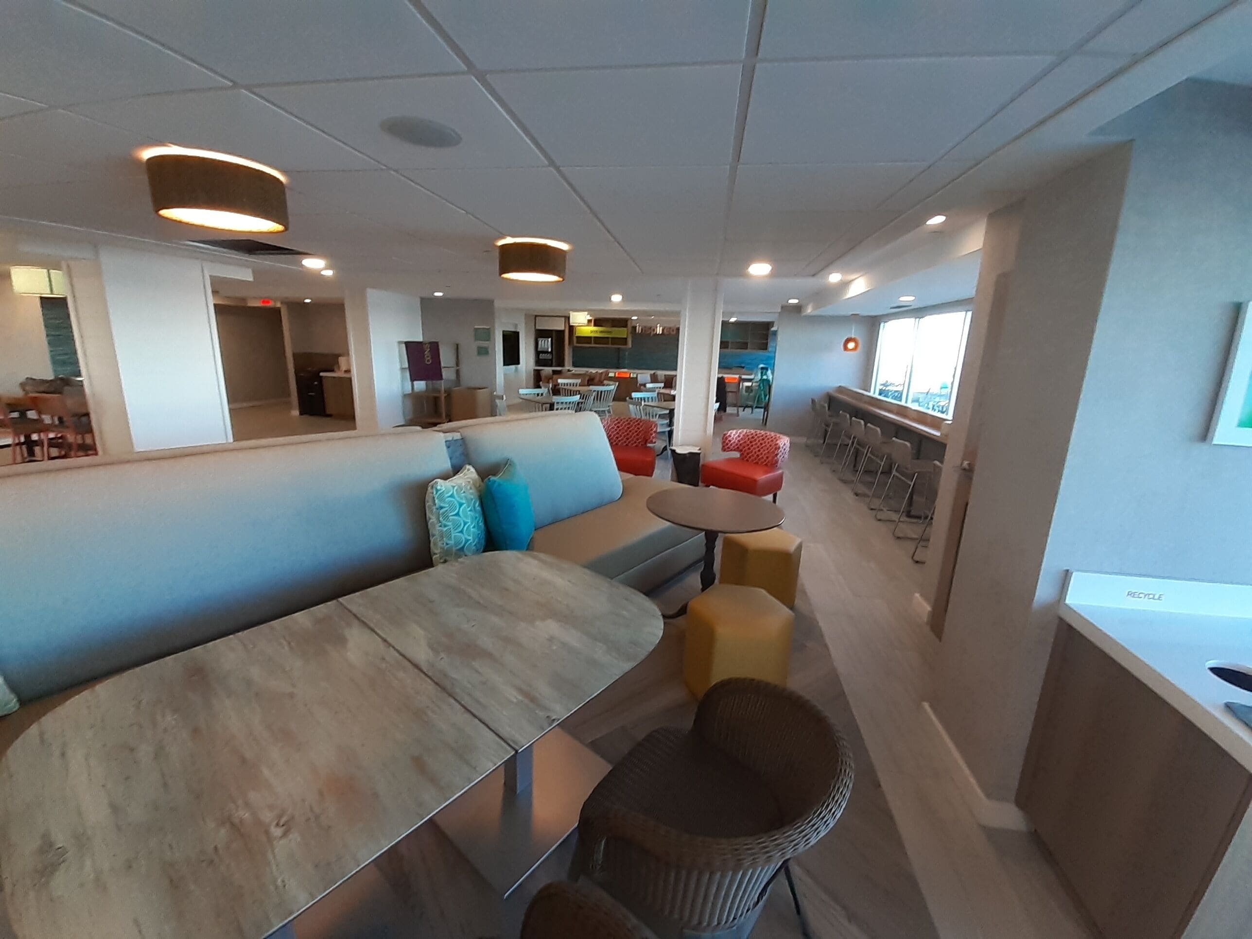 Um interior moderno com uma longa mesa comunitária, um sofá com almofadas coloridas e um bar com banquetas.