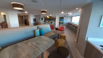 Um interior moderno com uma longa mesa comunitária, um sofá com almofadas coloridas e um bar com banquetas.