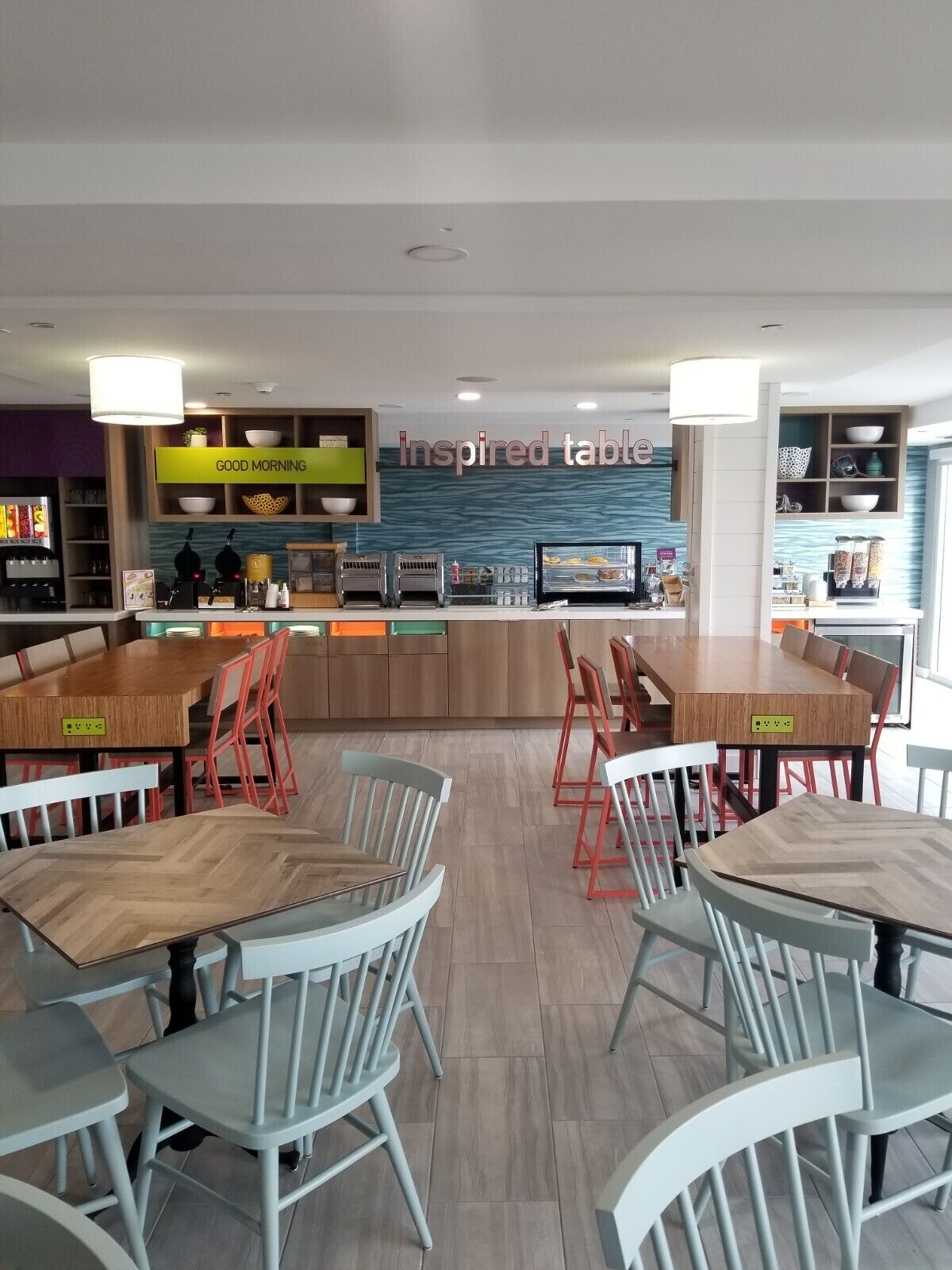 A modern restaurant with a central bar area, multiple seating options including booths and tables, and a visible menu board.