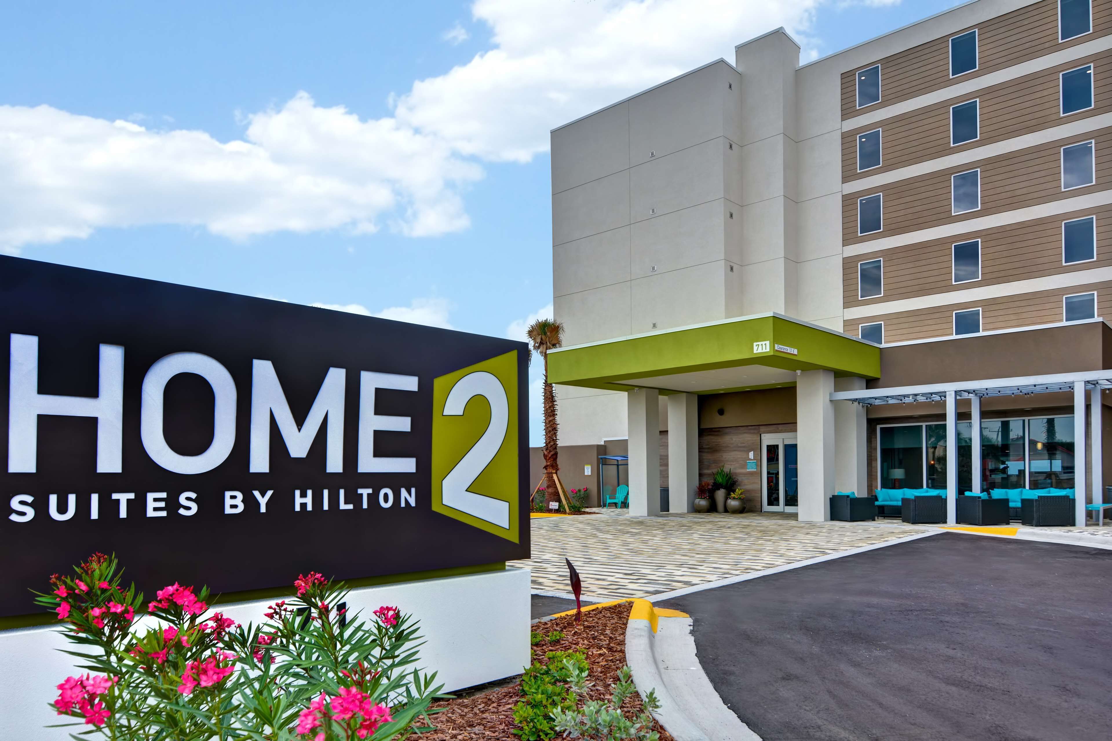 Entrada de hotel com uma placa indicando 'HOME 2 SUITES BY HILTON'.