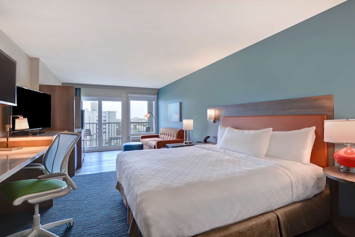 Une chambre d’hôtel avec un grand lit, un bureau avec une chaise, une télévision et une fenêtre donnant sur des immeubles.