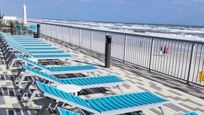 A beachside promenade with rows of blue lounge chairs and a metal railing overlooking the ocean.