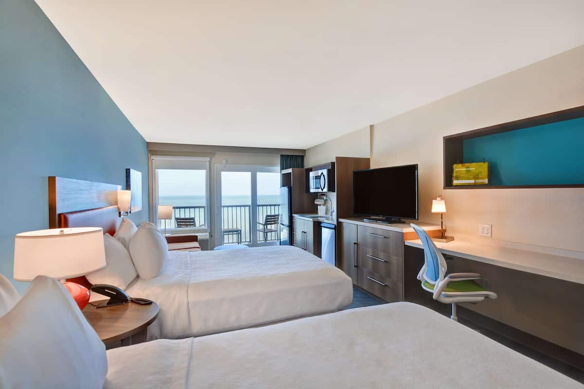Une chambre d’hôtel avec deux lits, un bureau avec une lampe, une télévision et un balcon avec vue.