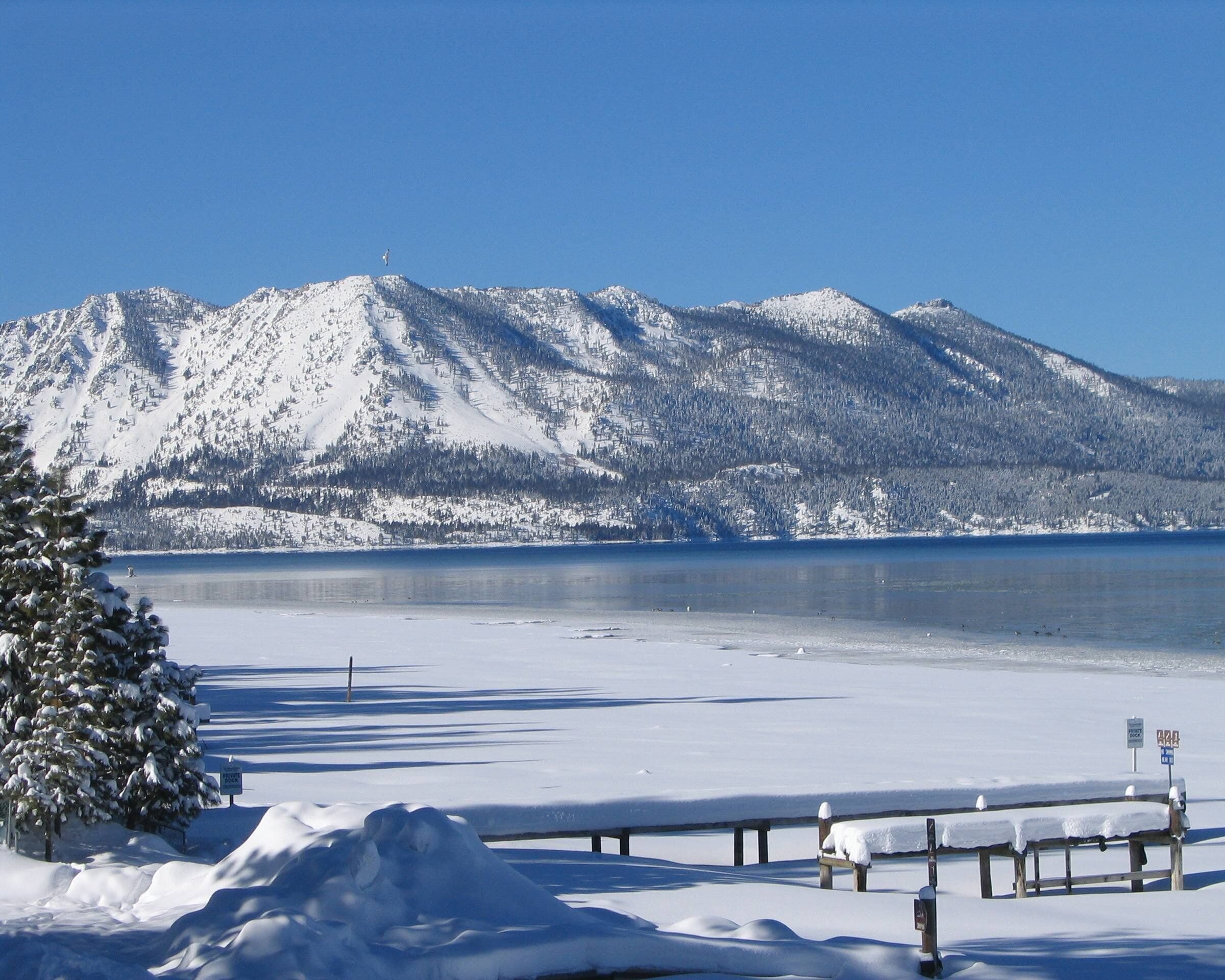 Um lago coberto de neve com montanhas ao fundo e um banco em primeiro plano.
