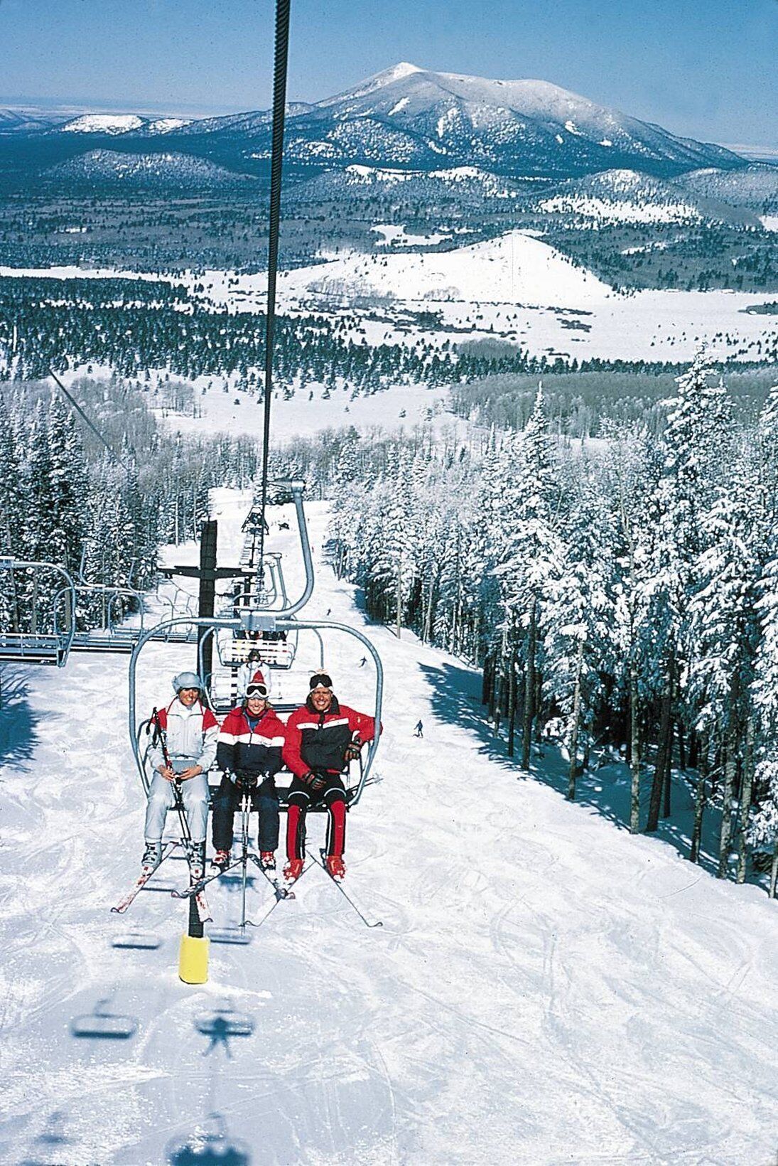 Hiihtohissi, jossa on kolme laskettelijaa punaisissa ja valkoisissa takeissa.