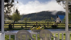 A covered porch with two white chairs, a flower arrangement, and a view of a rural landscape with a barn and forested hills. - Miller Tree Inn (Forks)