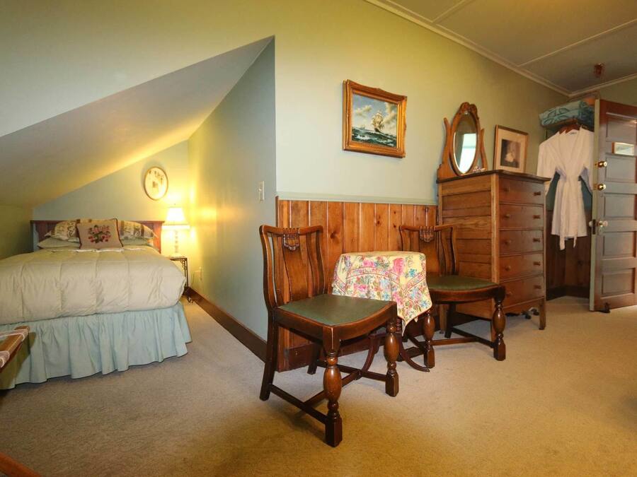 Een slaapkamer met een bed, een houten dressoir, een stoel, een tafel en een spiegel.