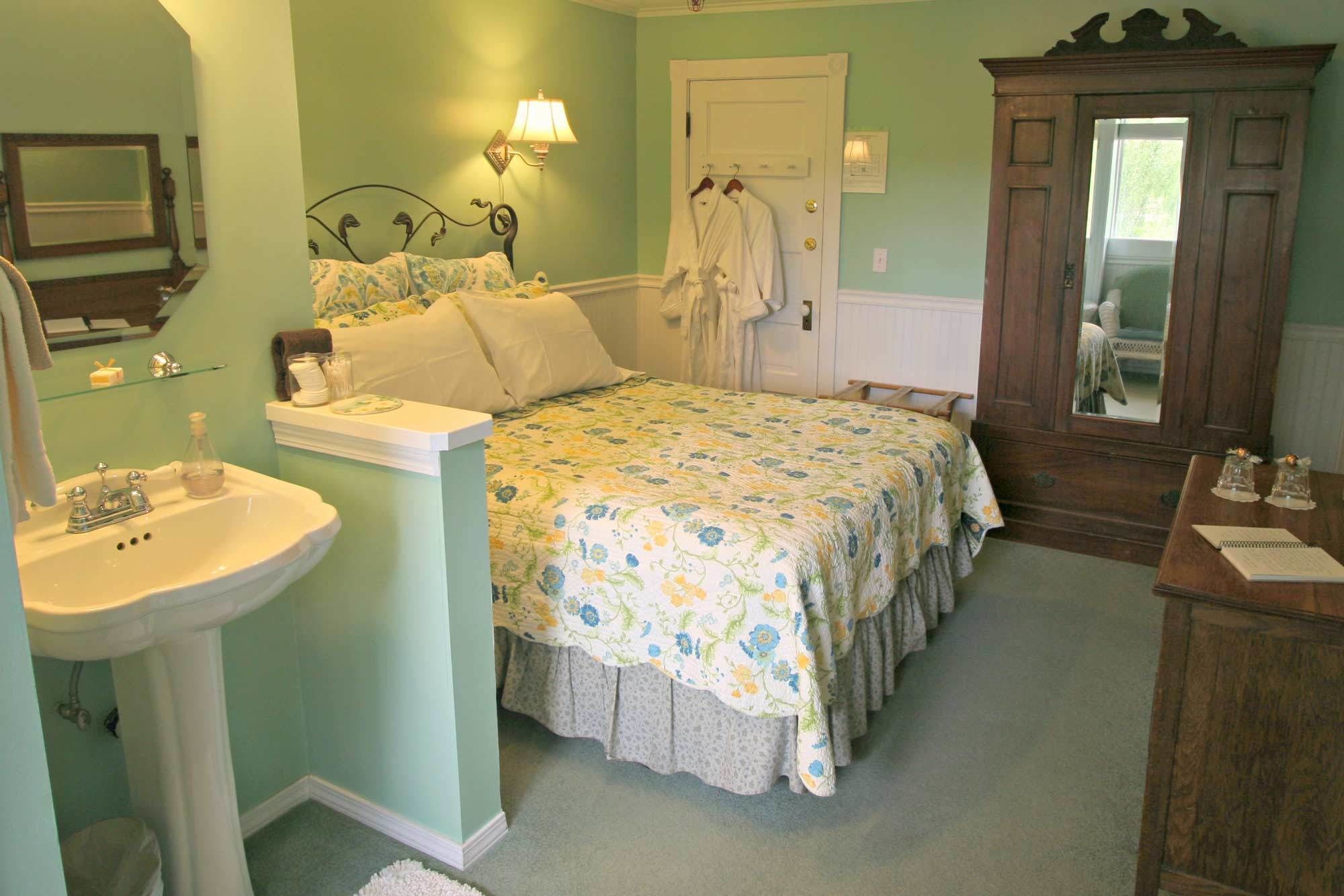 A bedroom with a bed, a bedside table, a mirror, a dresser, and a door.