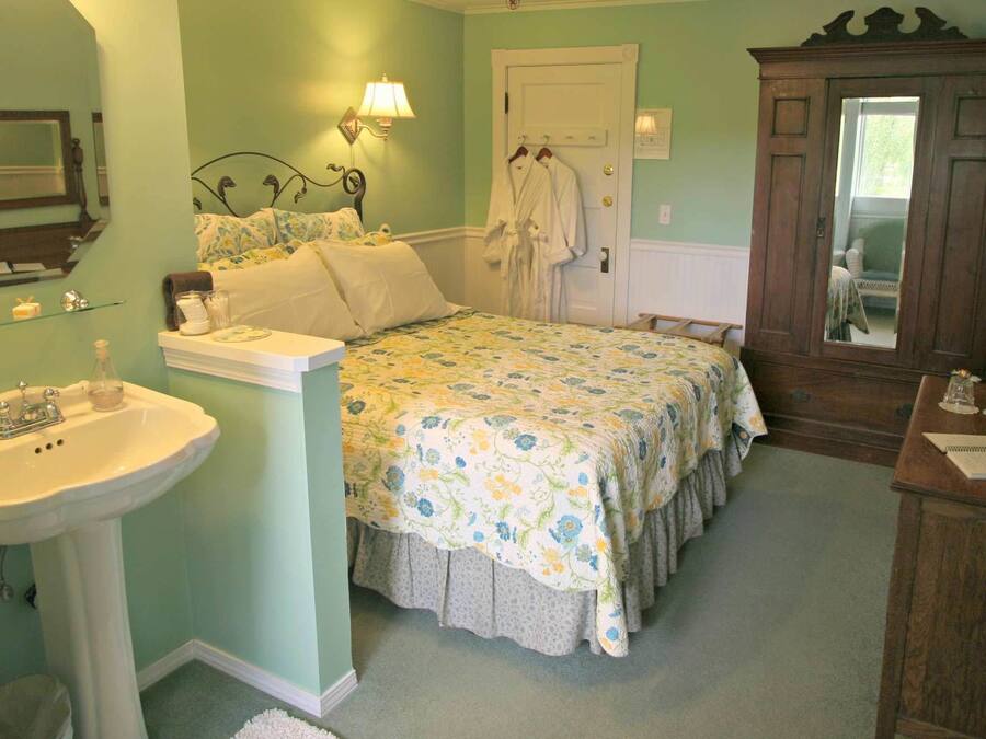 A bedroom with a bed, a bedside table, a mirror, a dresser, and a door.