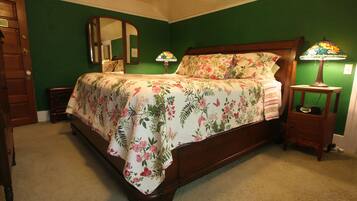 Een slaapkamer met een bloemenprint bedsprei, een houten hoofdbord, een nachtkastje met een lamp en een spiegel aan de muur.