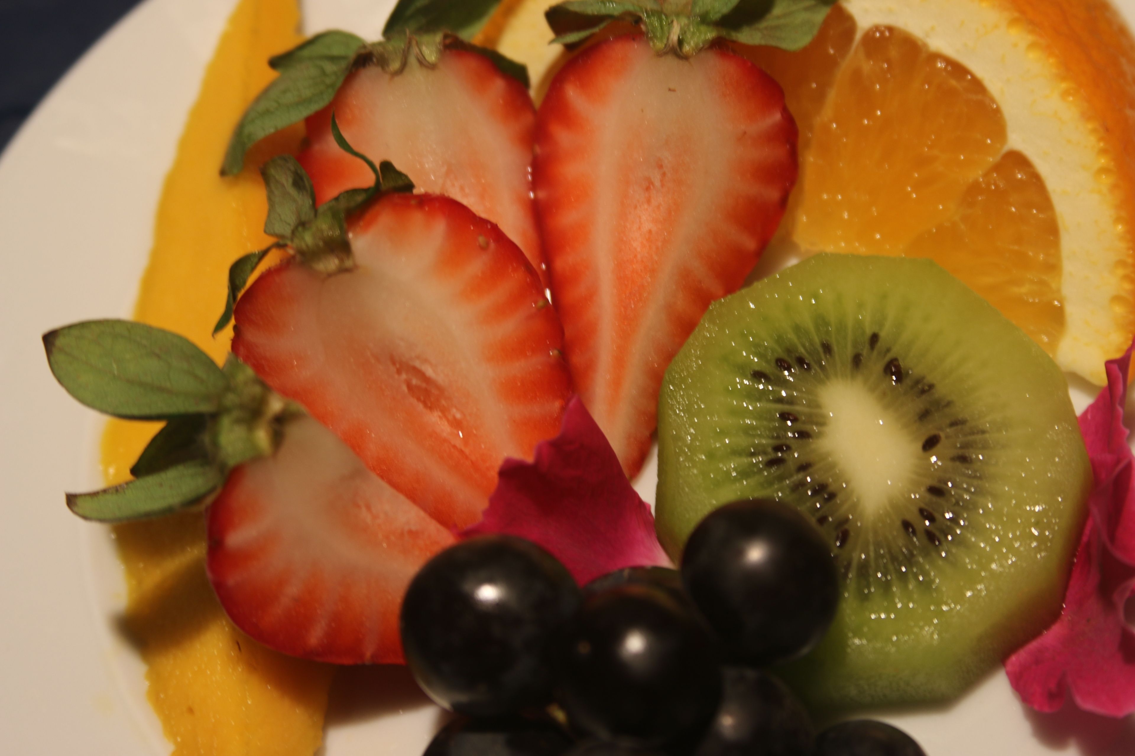 Une assiette de fruits comprenant des fraises, des kiwis, des raisins et des tranches d’orange.