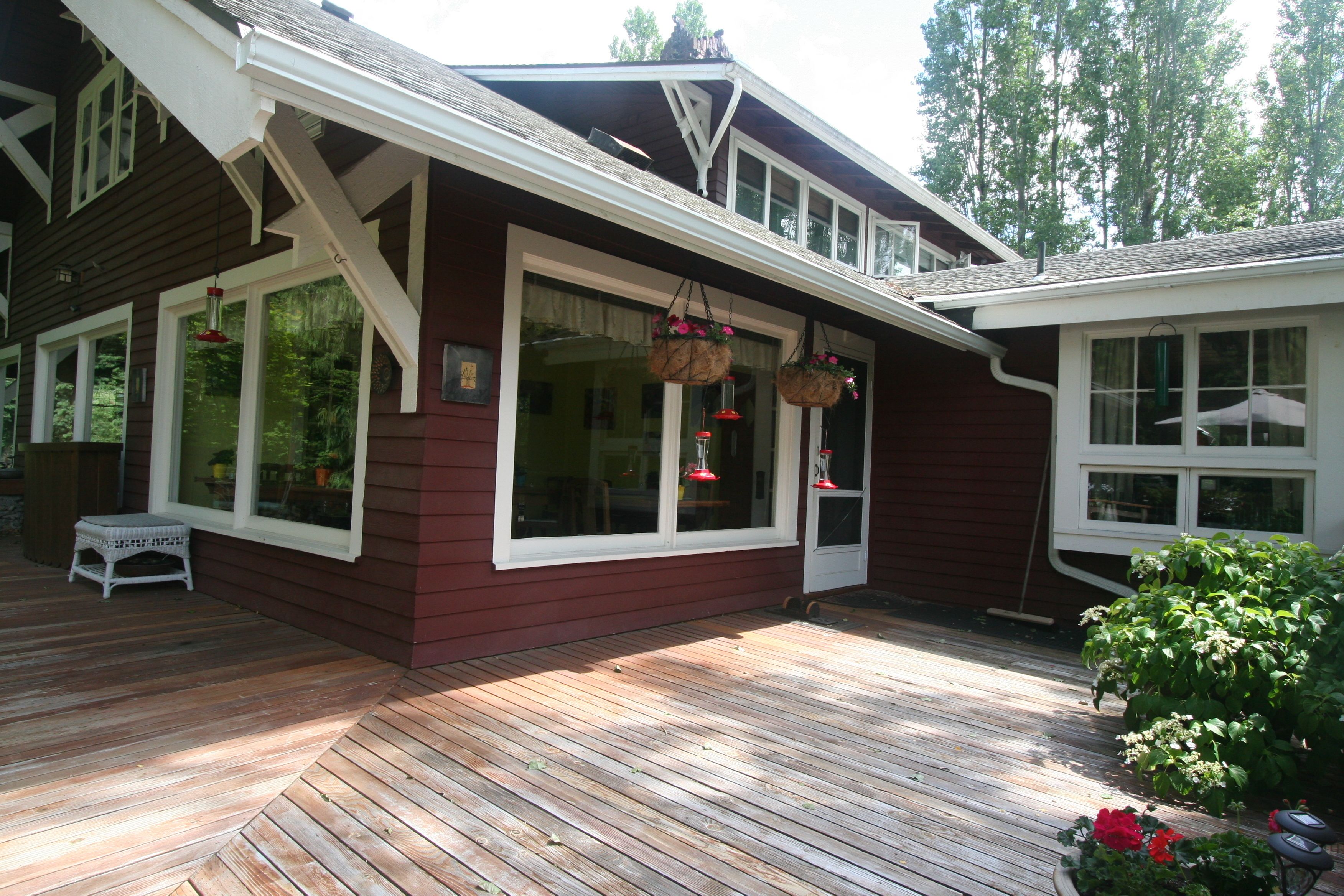 A wooden deck with a white bench, large windows, and hanging flower baskets.