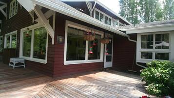 A wooden deck with a white bench, large windows, and hanging flower baskets.