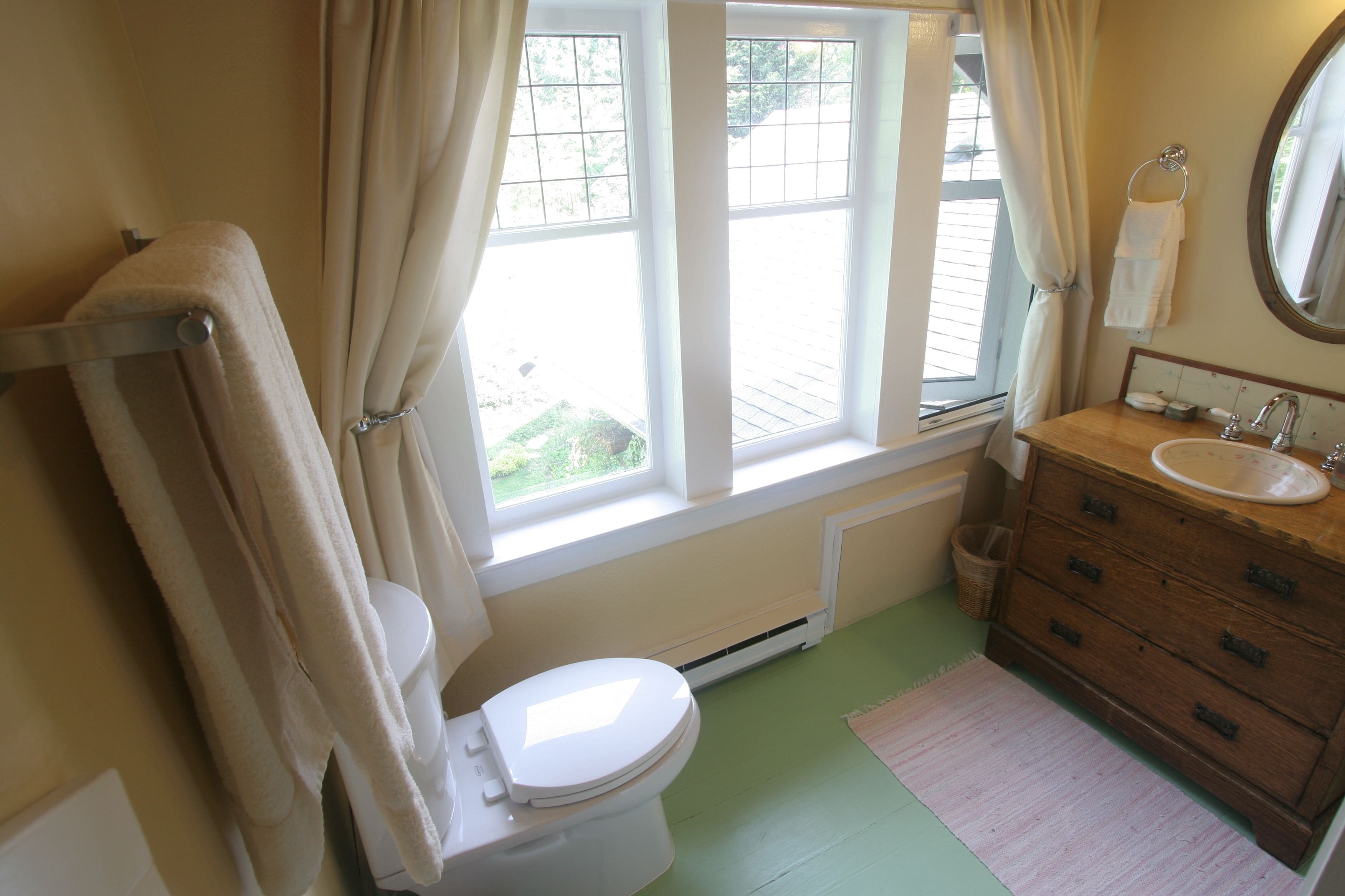A bathroom with a toilet, a sink, a wooden cabinet, and a window with curtains.