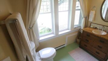 A bathroom with a toilet, a sink, a wooden cabinet, and a window with curtains.