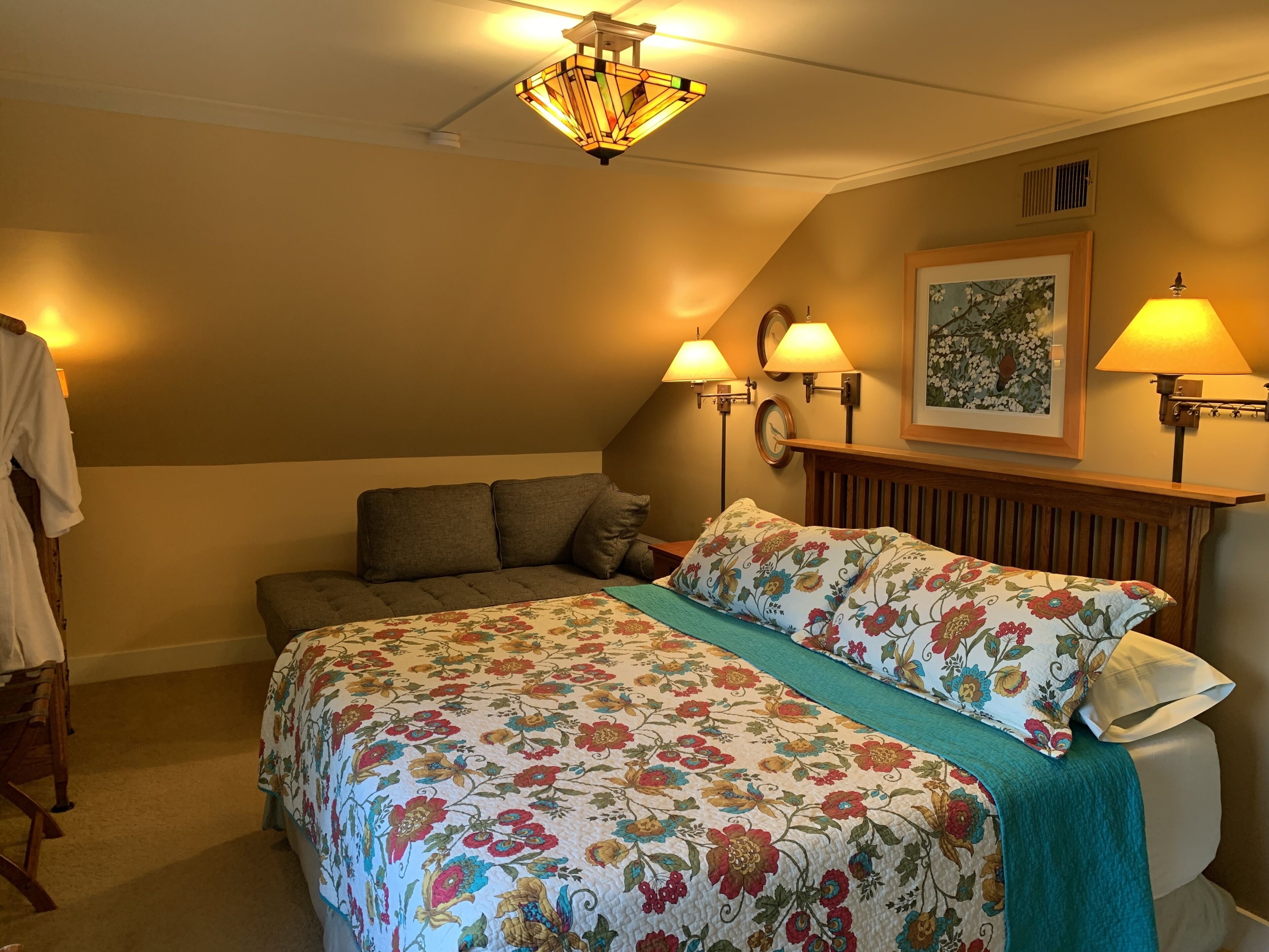 A bedroom with a bed, a nightstand, a lamp, a wall clock, and a framed picture.