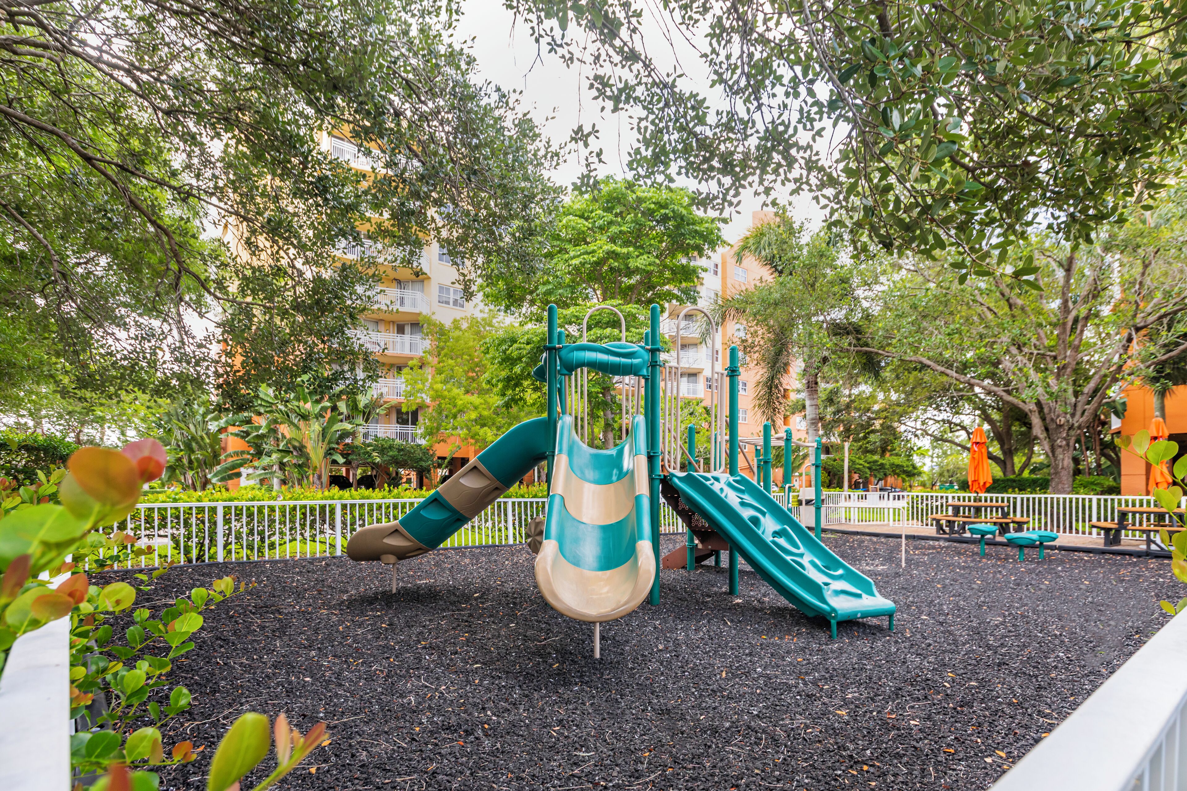 A playground with slides and climbing structures, surrounded by trees and a fence.