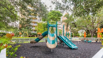 A playground with slides and climbing structures, surrounded by trees and a fence.