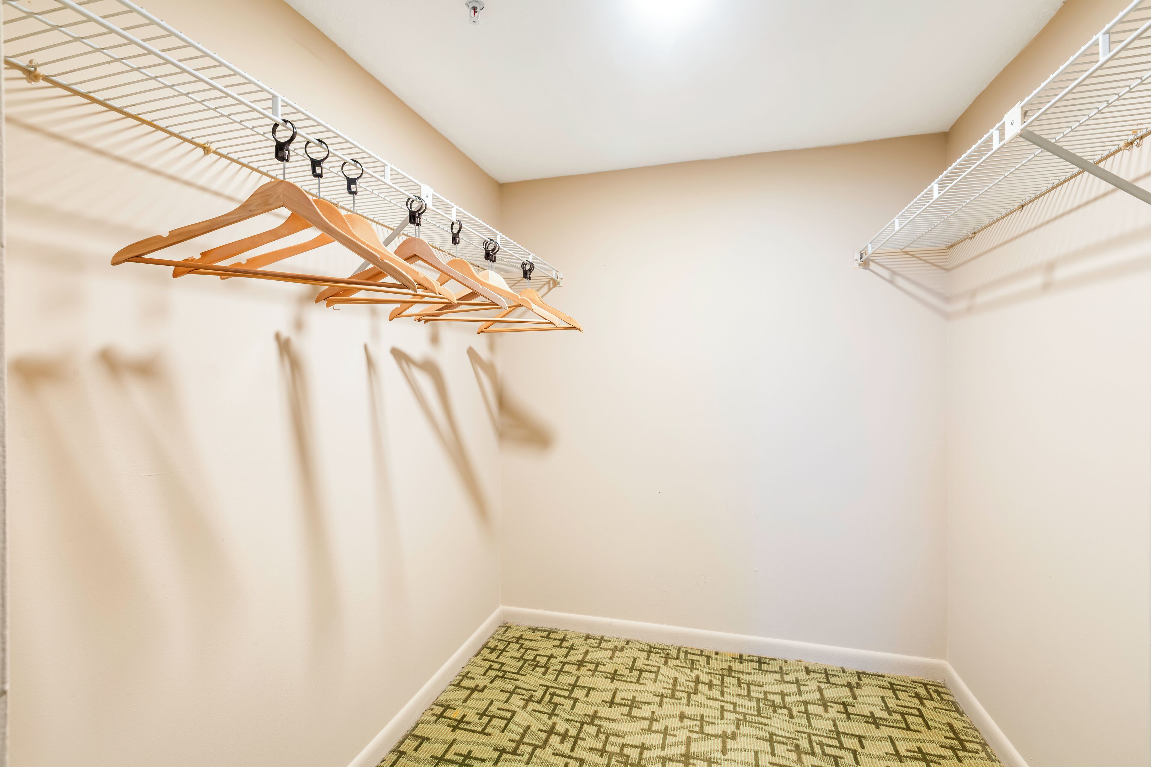 A corner of a room with a white ceiling, a wooden hanger rack, and a patterned rug.