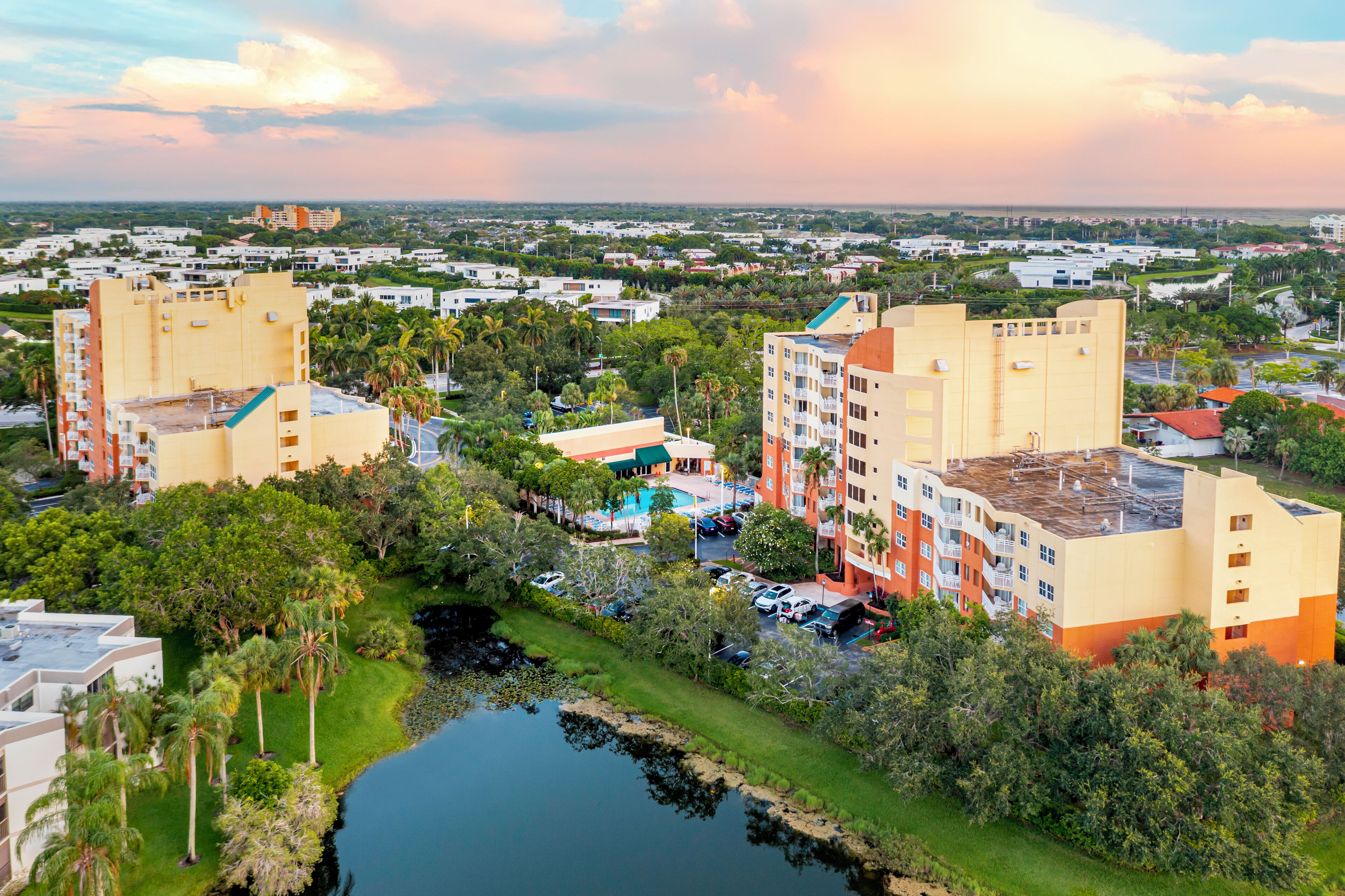 A multi-story hotel with a pool, surrounded by greenery and a body of water.