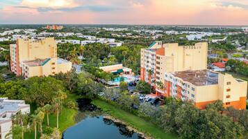 A multi-story hotel with a pool, surrounded by greenery and a body of water.