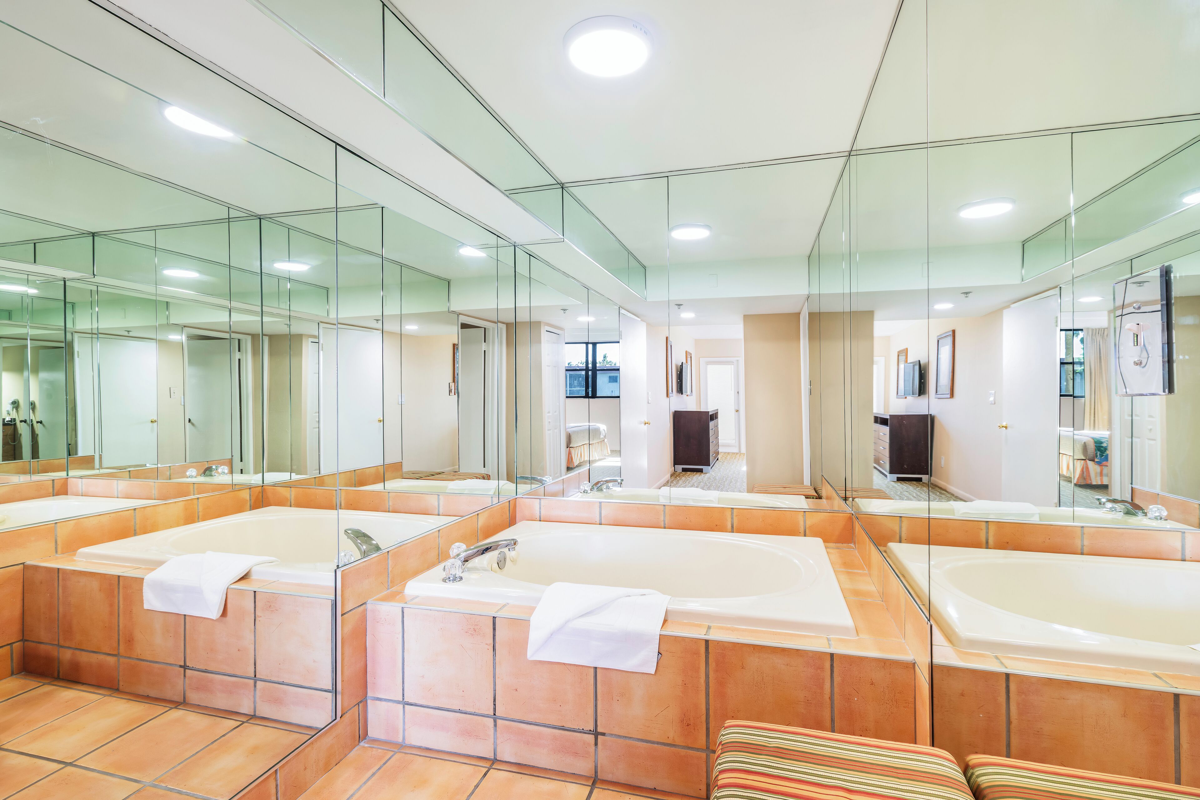 A modern bathroom with three large tubs, a glass shower enclosure, and a large mirror reflecting the space.