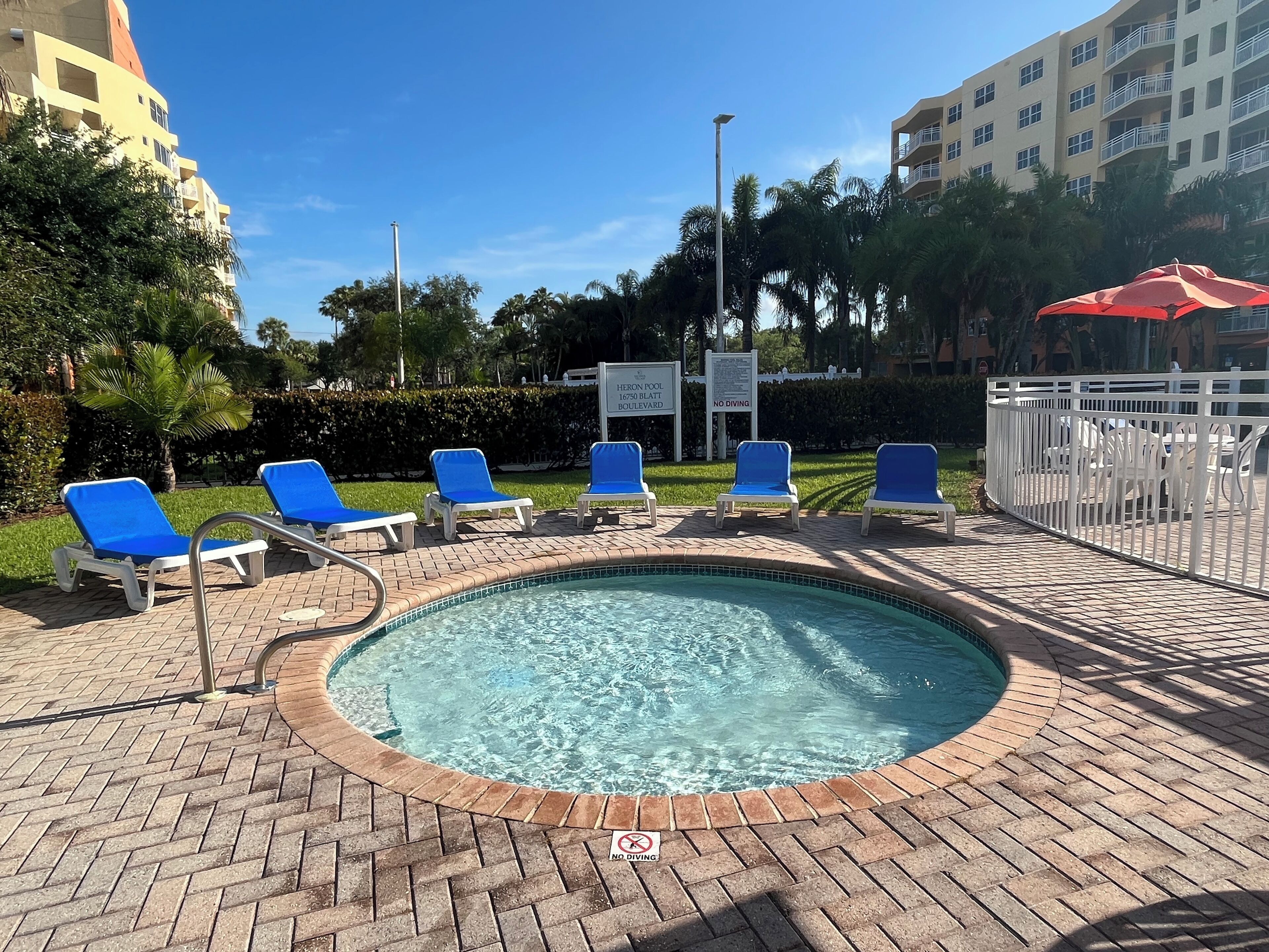 Un espace piscine avec des chaises longues bleues et un panneau indiquant « Il est interdit de plonger ».