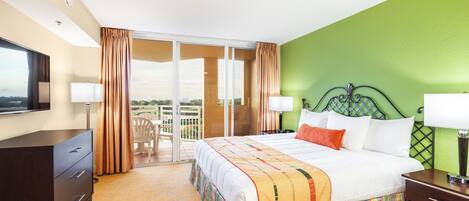A hotel room with a large bed, a desk, a chair, and a balcony with curtains.