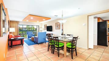 A dining area with a table set for four, surrounded by chairs with green cushions, a blue armchair, and a red sofa.