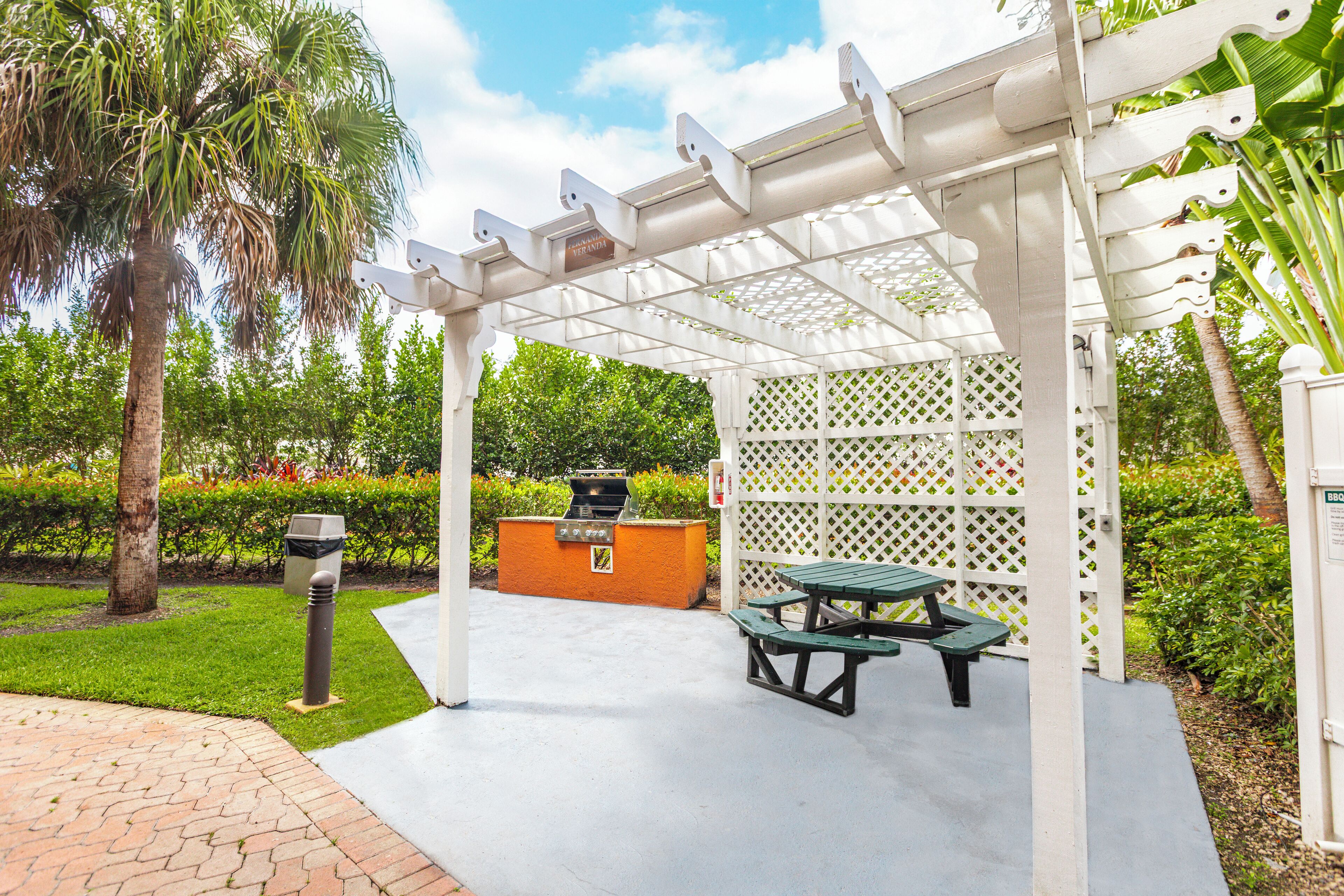 An outdoor patio with a grill, picnic table, and white lattice structure.