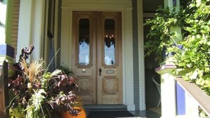 A wooden front door with a small porch and a potted plant with a pumpkin.