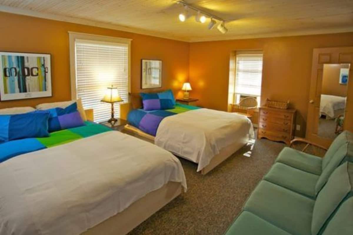 A hotel room with two beds, a dresser, a chair, and a lamp.