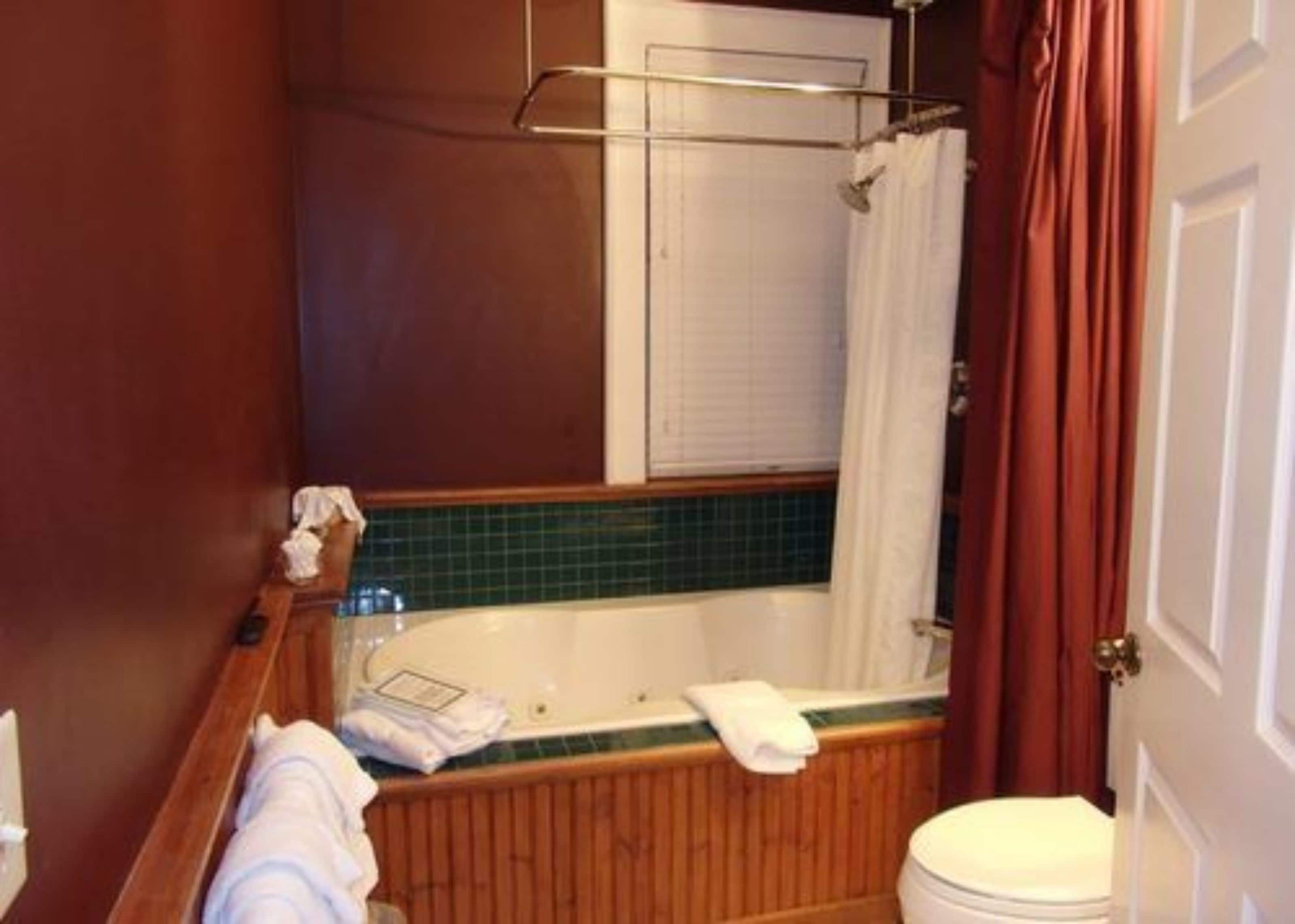 Une salle de bain avec une baignoire en bois, des toilettes blanches et un rideau de douche.