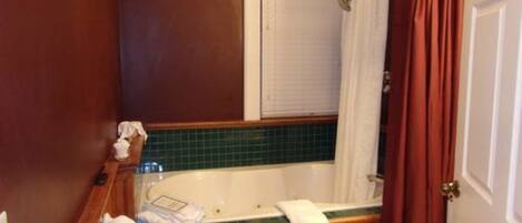 Un baño con una bañera de madera, un inodoro blanco y una cortina de ducha.