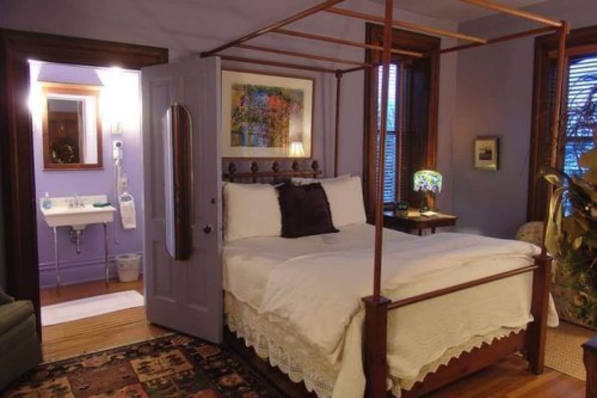 A four-poster bed in a room with a wooden floor, a small bedside table, and a nightstand.