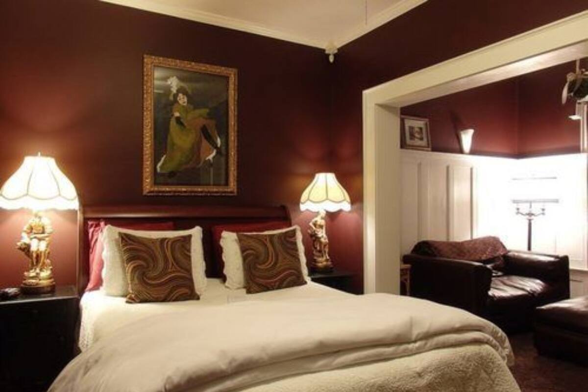 A hotel room with a large bed, two bedside lamps, a painting on the wall, and a view of the outside.
