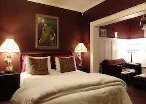 A hotel room with a large bed, two bedside lamps, a painting on the wall, and a view of the outside.