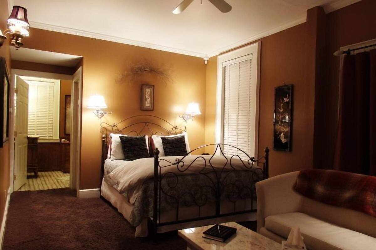 A hotel room with a bed, a sofa, a small table, and a ceiling fan.