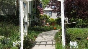A garden pathway leading to a white pergola with an American flag.