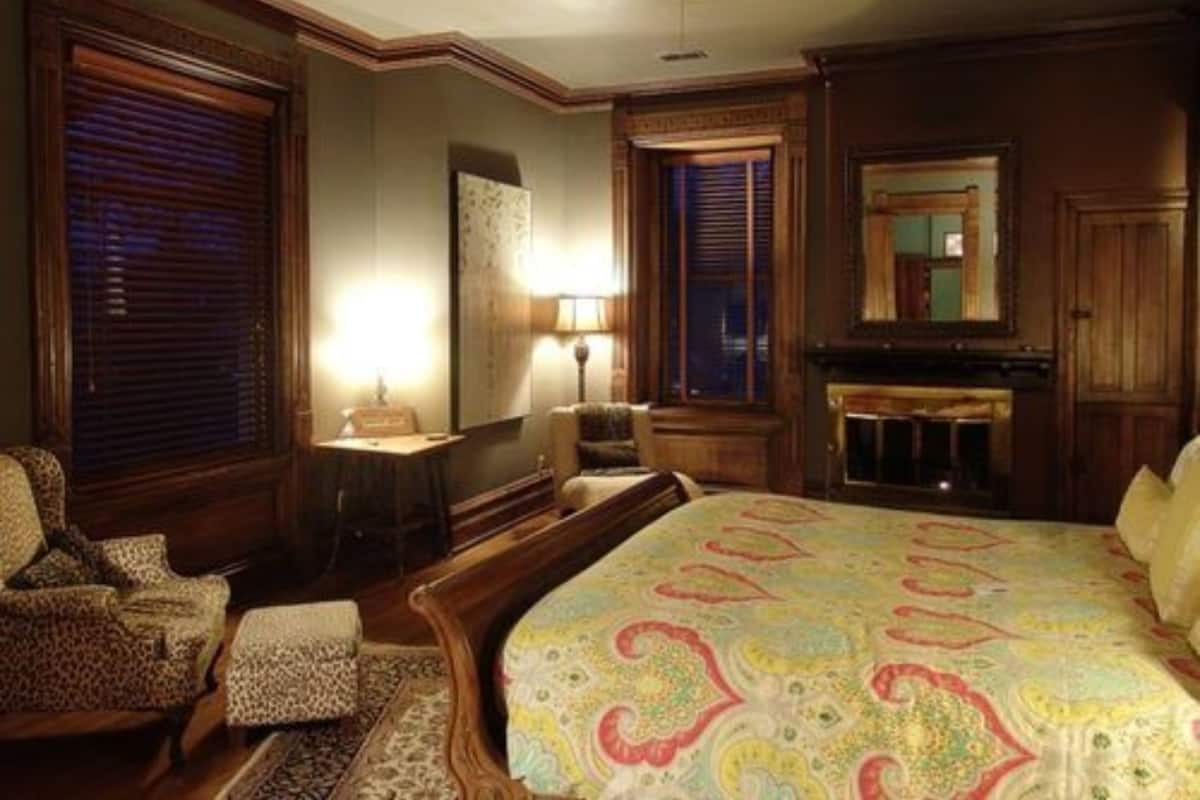 A traditional bedroom with a large bed, a wooden dresser, a chair, and a fireplace.