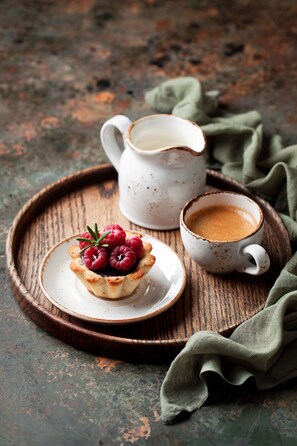 A rustic wooden tray with a small white cup of coffee and a pastry with raspberries on a green cloth.