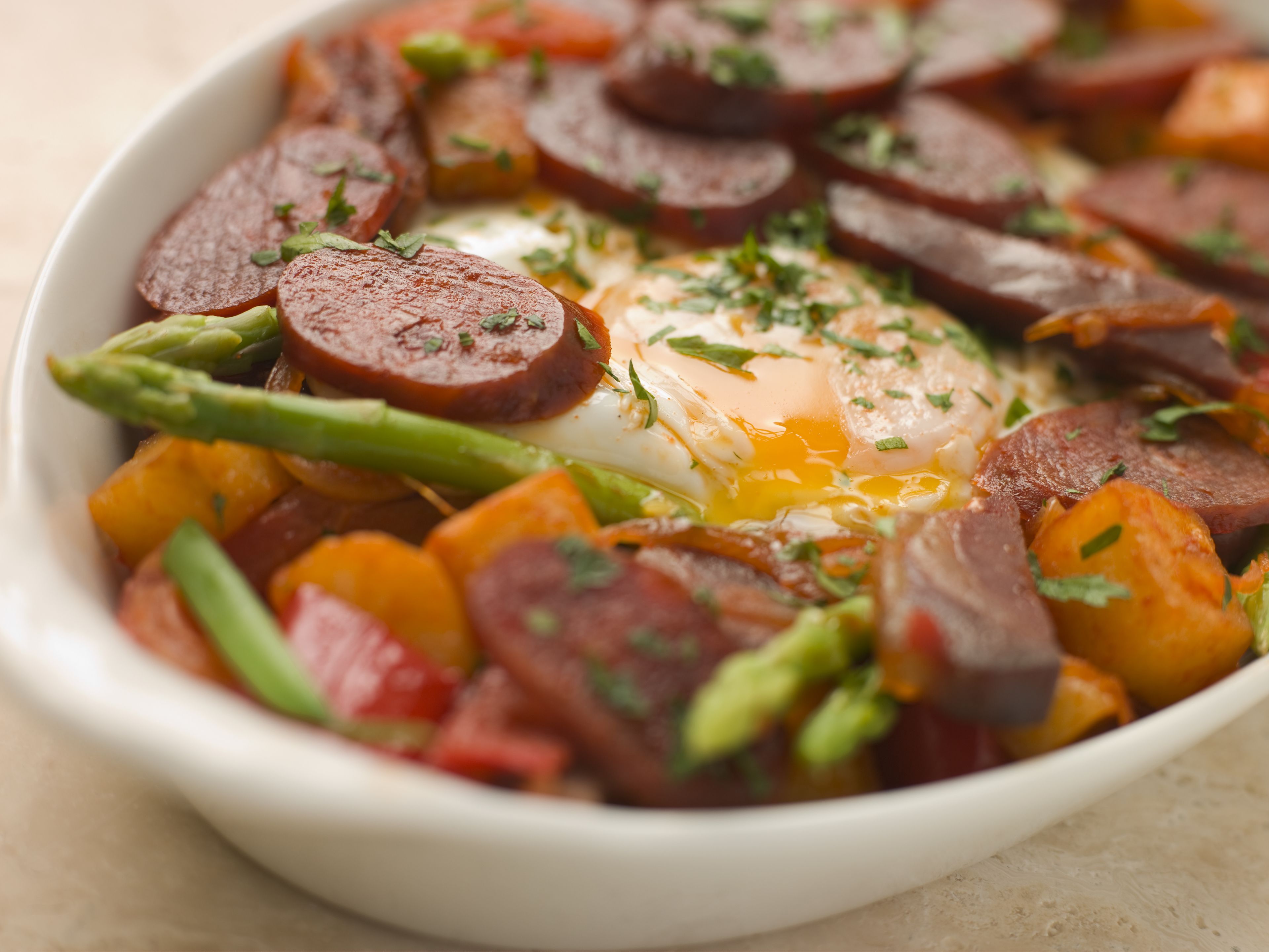 Un bol contenant des aliments, notamment des saucisses en tranches, des légumes et un œuf poché.