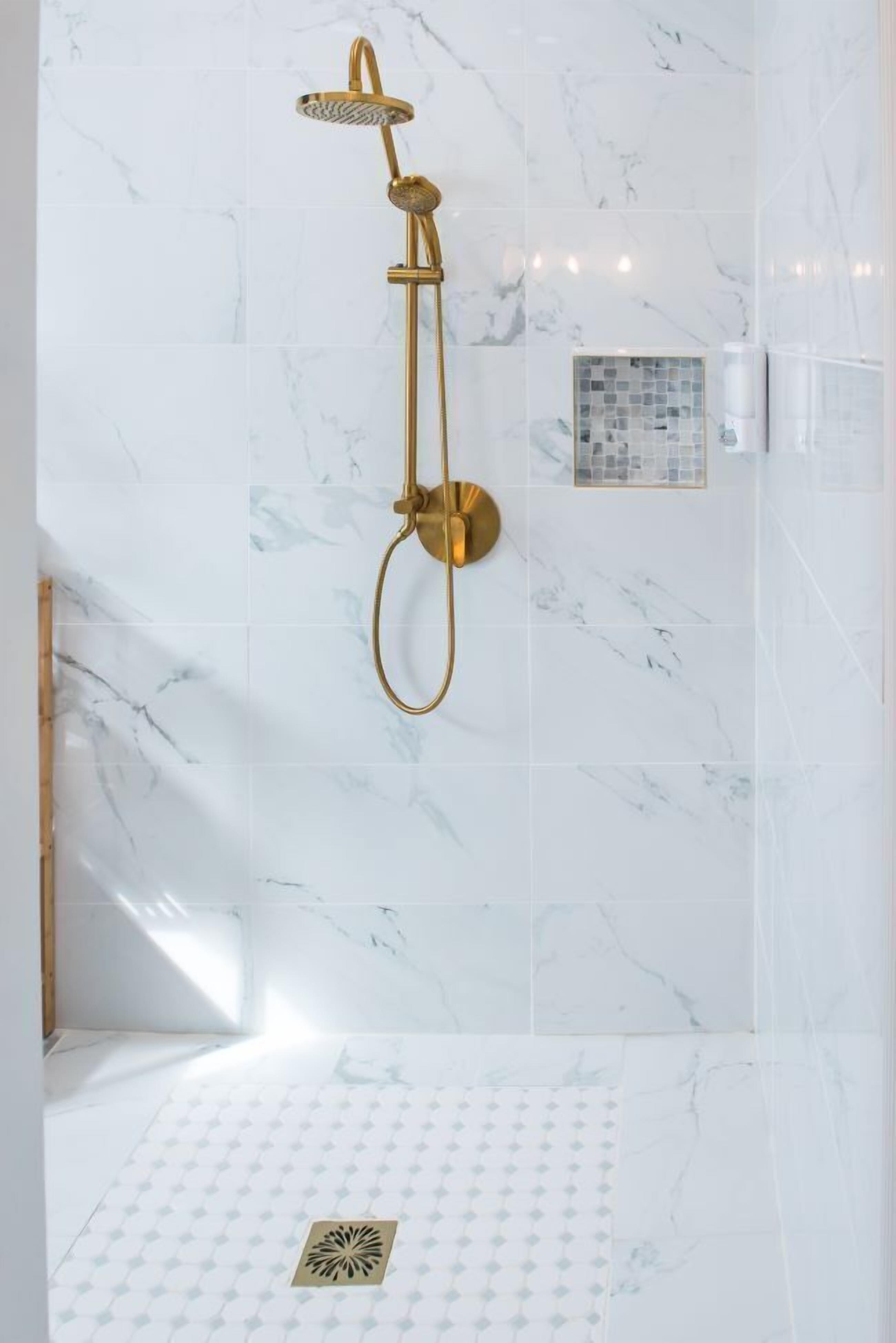 Una ducha con detalles dorados en un baño con baldosas de mármol blanco.