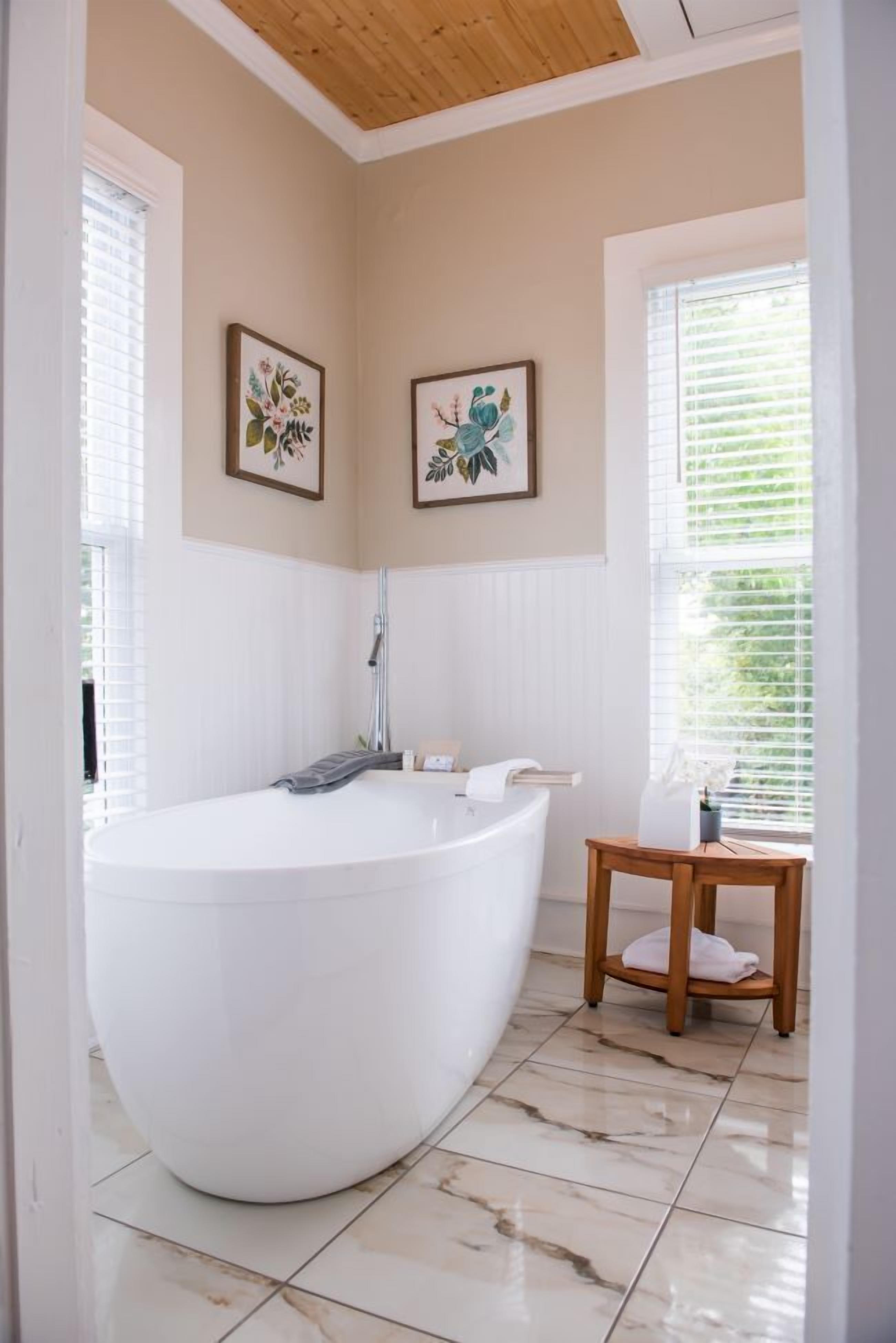 A bathroom with a freestanding bathtub, a wooden stool, and two framed floral paintings on the wall.